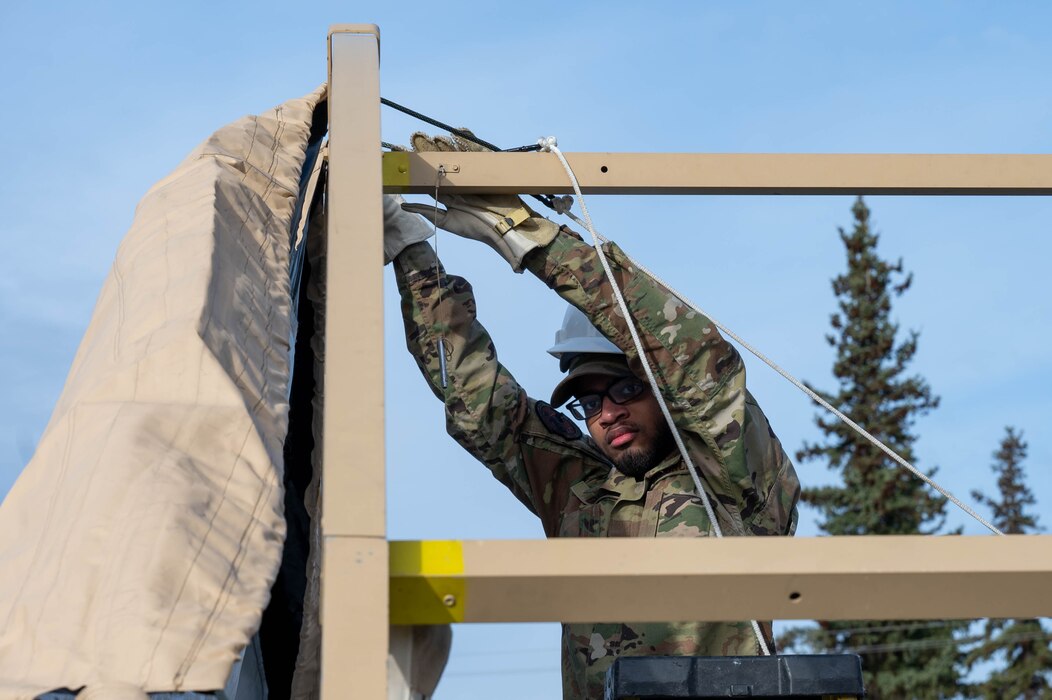 U.S. Air Force Airman 1st Class Mychal Daniels, 354th Force Support Squadron food service technician, clips the top of a tent cover during a Ready Raven Team exercise to bolster Agile Combat Employment at Eielson Air Force Base, Alaska, May 2, 2024.