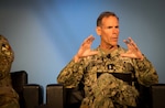 A man in a camouflage military uniform with two stars on the chest sits on a chair looking off screen while gesturing with his hands.