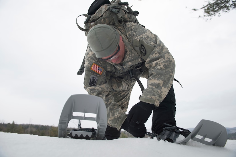 A man works a clasp to put on snowshoes in the snow.