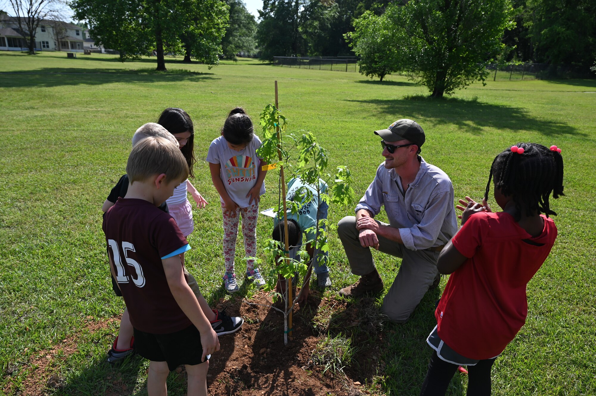 A group of children are accompanied by 14 CES Natural Resources personnel during planting of new heritage tree saplings.