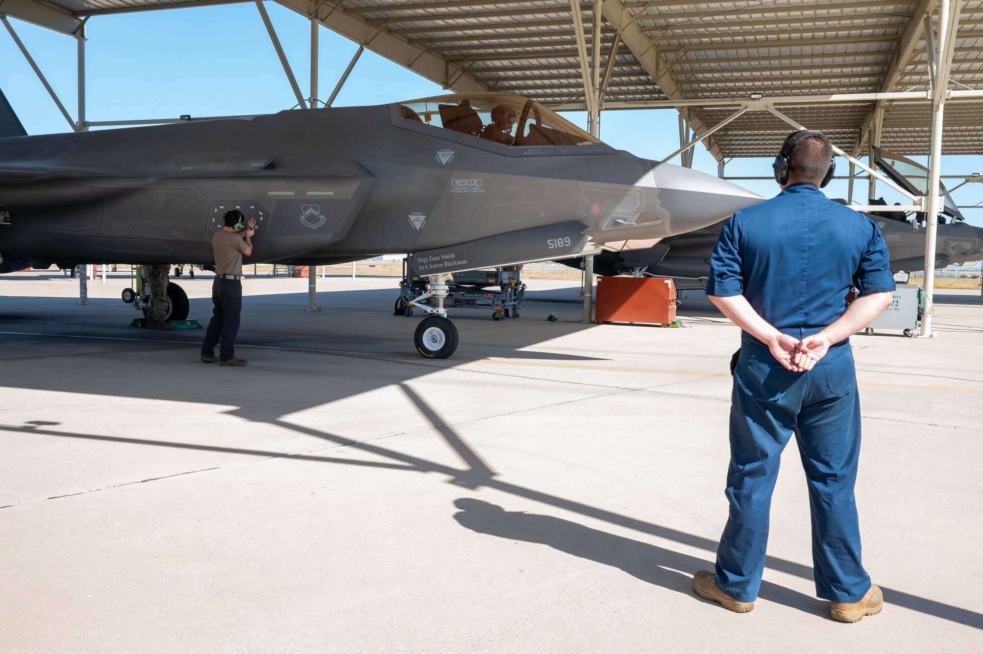 U.S. Air Force Staff Sgt. Tristen Gilliland, 308th Aircraft Maintenance Unit crew chief, observes as Senior Airman Daniel Oates, 308th AMU avionics technician, secures a panel on an F-35 Lightning II, May 9, 2024, at Luke Air Force Base, Arizona.
