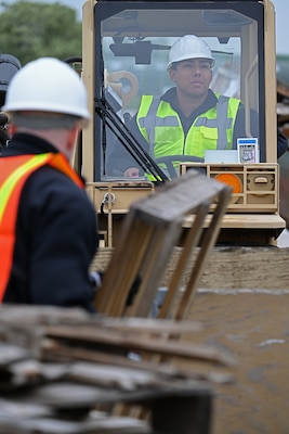 A sailor in safety gear operates a forklift.