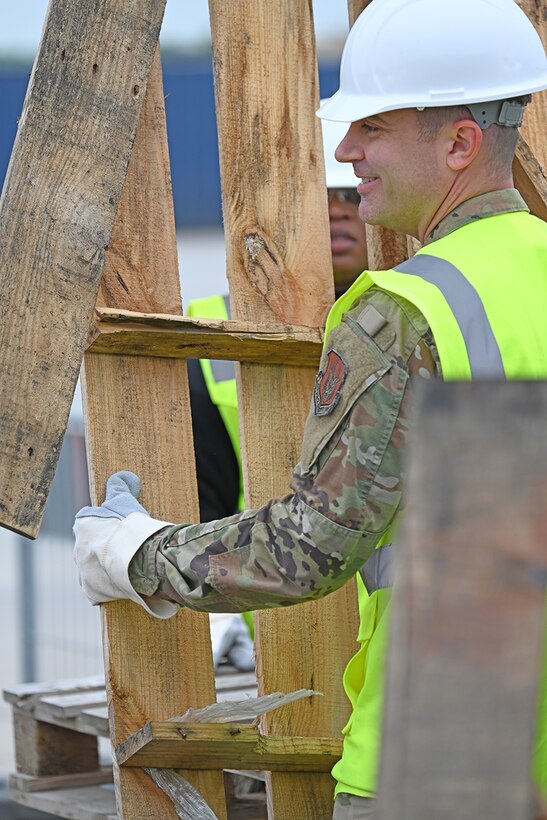 An airman in safety gear lugs a wood pallet.