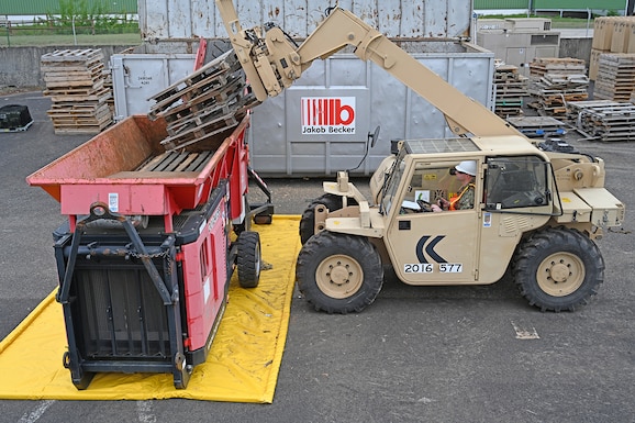 A sailor driving material handling equipment loads wood pallets into an industrial shredder.