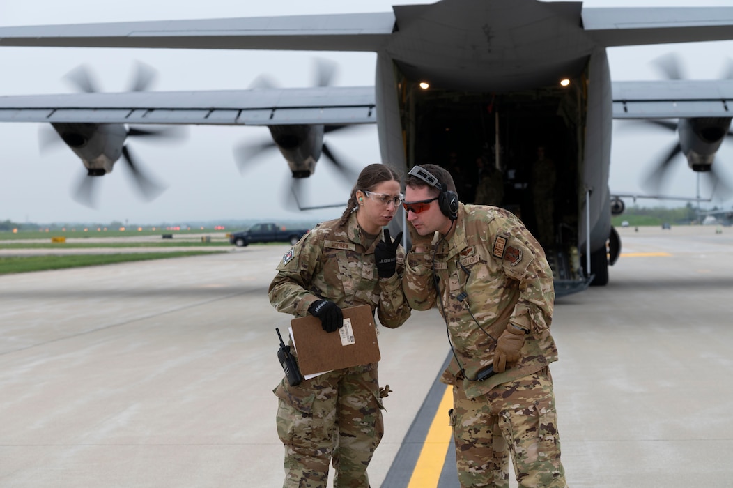 a woman speaks to a man on a flightline behind an aircraft