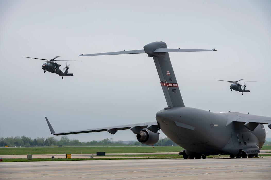 two helicopters fly by a cargo aircraft