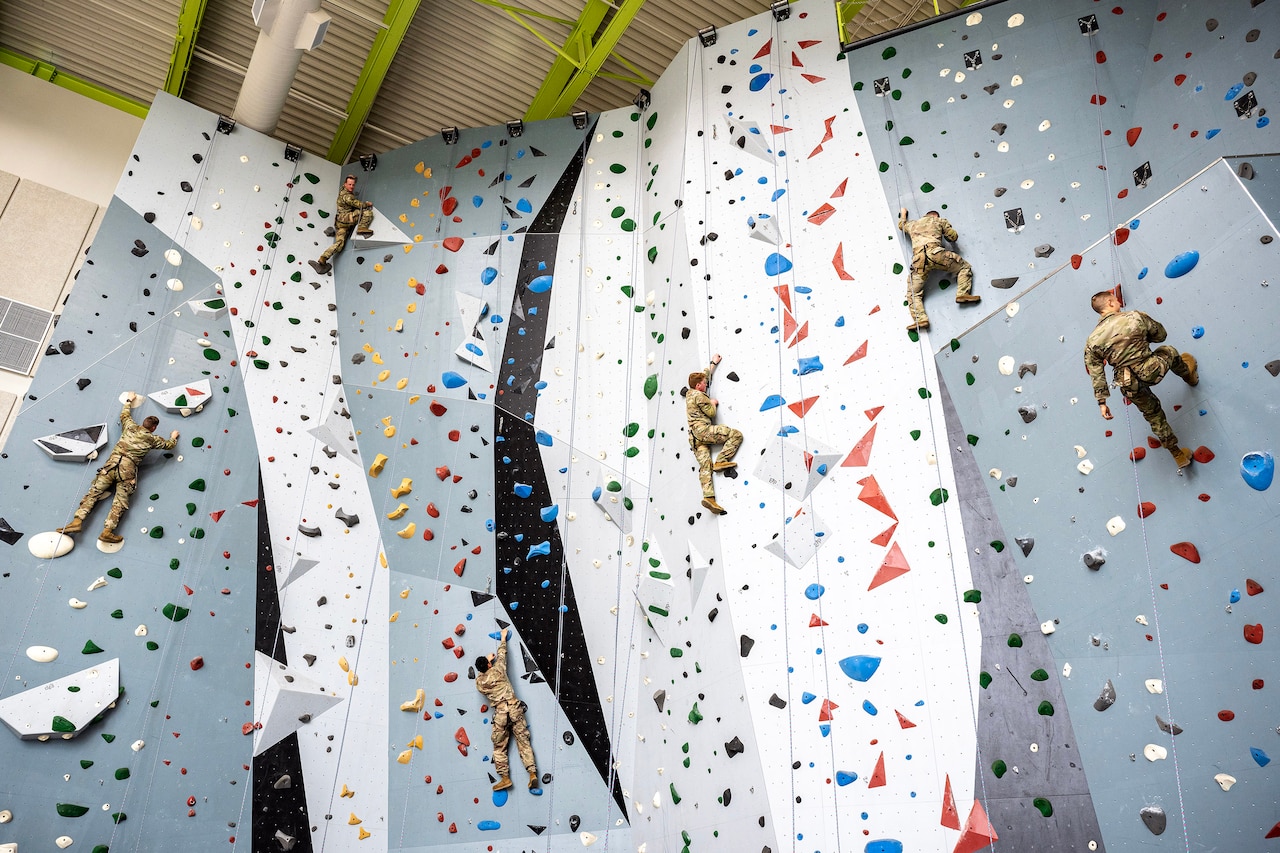Six people scale the side of a huge indoor rock wall.