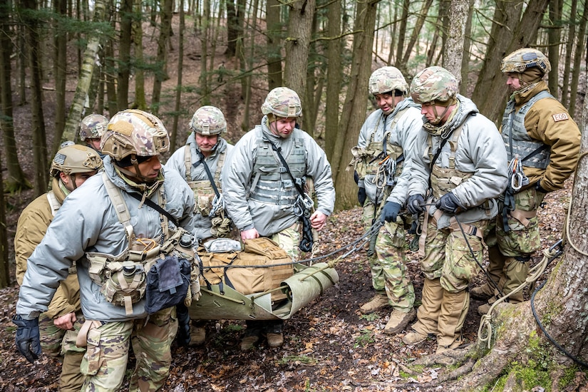 Several men carry a litter filled with backpacks up a steep hill.