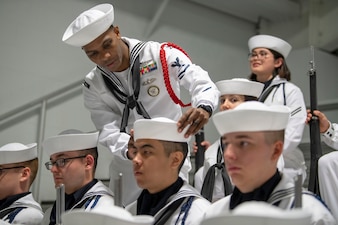 ABH Aviation Boatswain's Mate (Handling) Lauret Price fixes a recruit's cover inside Midway Ceremonial Drill Hall before a Recruit Training Command pass in review graduation ceremony