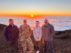 A group of individuals pose atop a mountain in Hawaii.