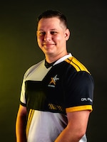 Man with multi-colored polo stands in front of a dark background.