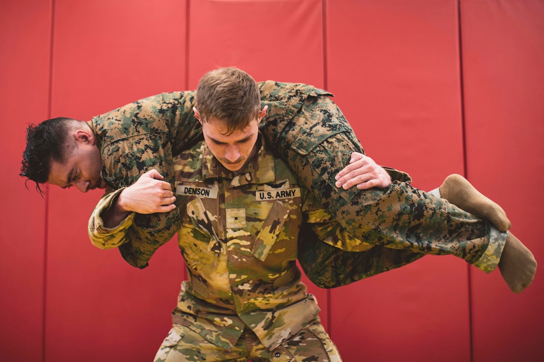 A soldier holds a fellow soldier behind their back over the shoulders to do a squat.