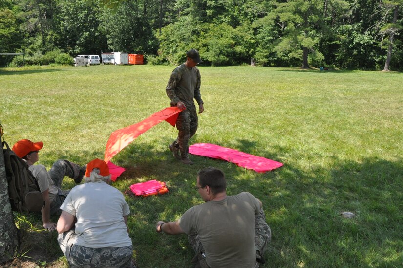 U.S. Air Force Tech. Sgt. Sam Neitzer, 305th Operations Support Squadron Survival, Evasion, Resistance and Escape Tactics noncommissioned officer in charge, constructs a Ground to Air Signal using brightly colored signal paulins during a lesson for Civil Air Patrol members at Hawk Mountain Ranger School, Kempton, Pa., July 2022. Neitzer is credited with playing a part in the survival of CAP pilots 1st Lt. Alysia Larson, West Bay Composite Squadron education and training officer, and Capt. Paul Larson, West Bay Composite Squadron health services officer, when their 1961 Piper Comanche aircraft lost power and went down into Narragansett Bay, R.I., March 30, 2024. Alysia Larson is pictured in the photo seated in the chair and wearing an orange hat. (Courtesy photo)