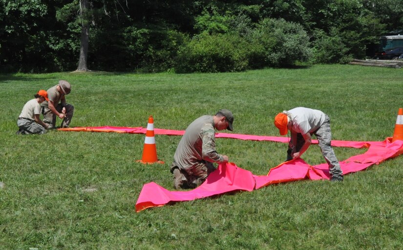 U.S. Air Force Tech. Sgt. Sam Neitzer, 305th Operations Support Squadron Survival, Evasion, Resistance and Escape Tactics noncommissioned officer in charge, instructs Civil Air Patrol members in constructing a Ground to Air Signal using brightly colored signal paulins during a lesson at Hawk Mountain Ranger School, Kempton, Pa., July 2022. Neitzer is credited with playing a part in the survival of CAP pilots 1st Lt. Alysia Larson, West Bay Composite Squadron education and training officer, and Capt. Paul Larson, West Bay Composite Squadron health services officer, when their 1961 Piper Comanche aircraft lost power and went down into Narragansett Bay, R.I., March 30, 2024. Alysia Larson is pictured in the photo wearing an orange hat and kneeling to assist with the signal paulin. (Courtesy photo)