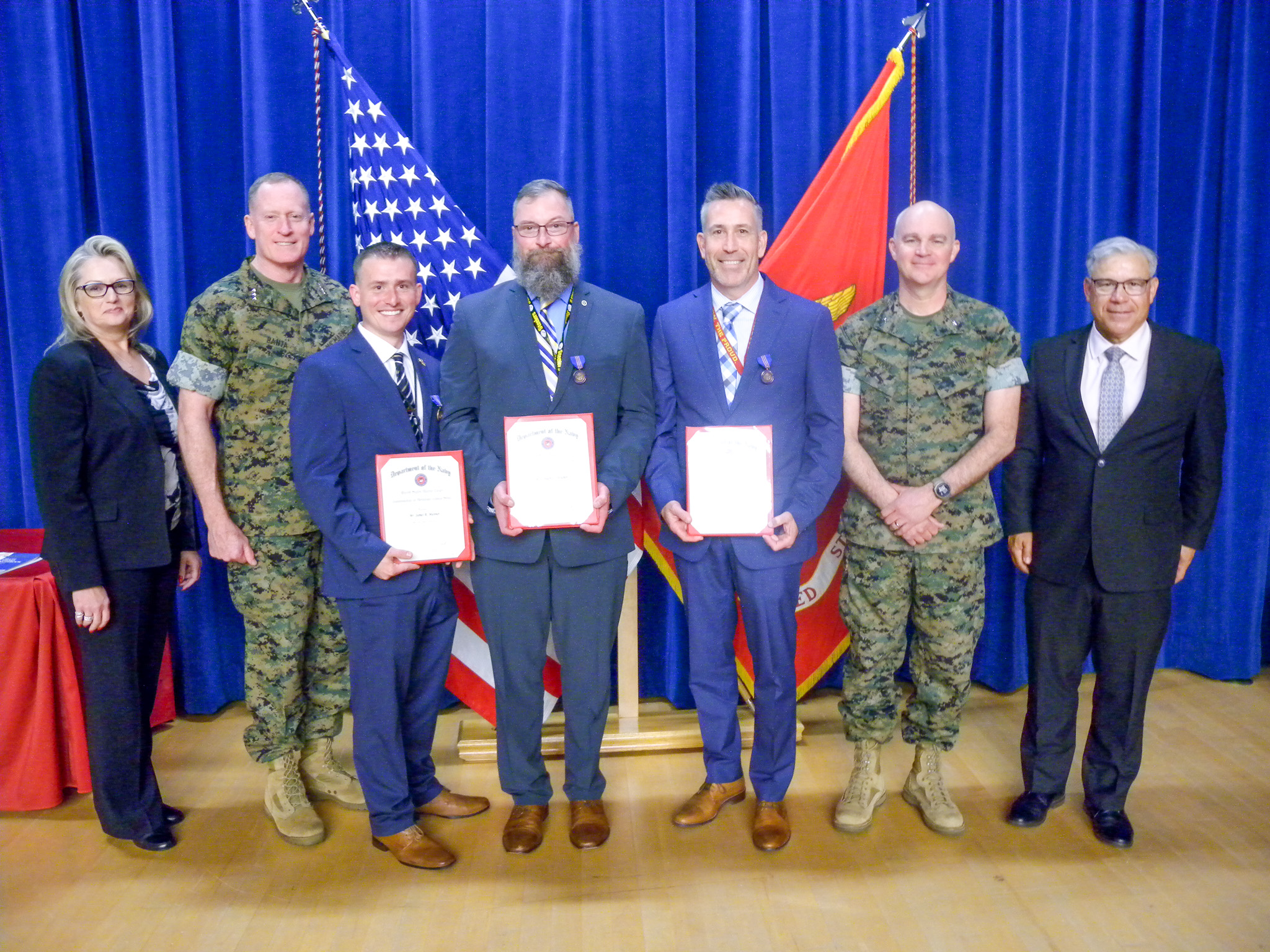 A group of men and women, three men in the center holding plaque awards.