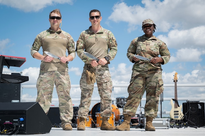 Three airmen pose with awarded knives on stage.