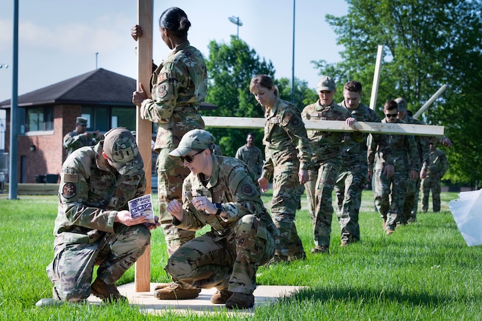 Airmen look at manual while others carry planks of wood in the background.