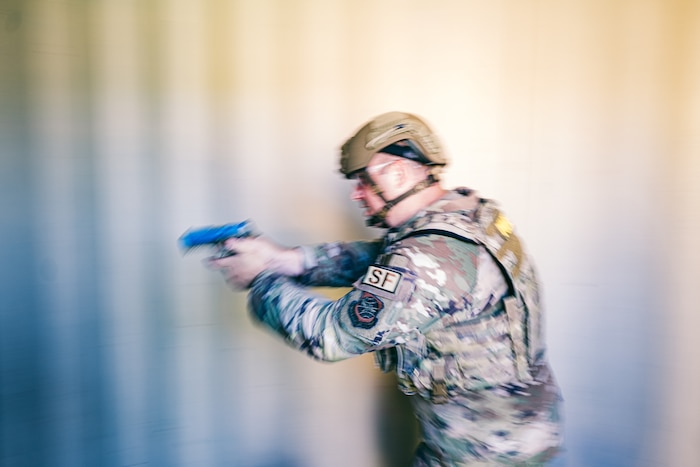 An airmen aims weapon down hallway in front of a metal wall.