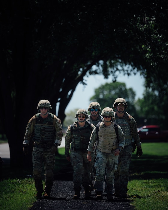 5 Airmen walk in uniform and helmets while competing in base readiness challenge.