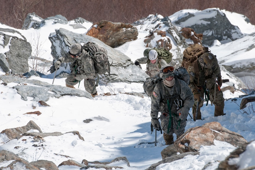 Four people in winter gear and heavy rucksacks climb up a snow-covered mountain.