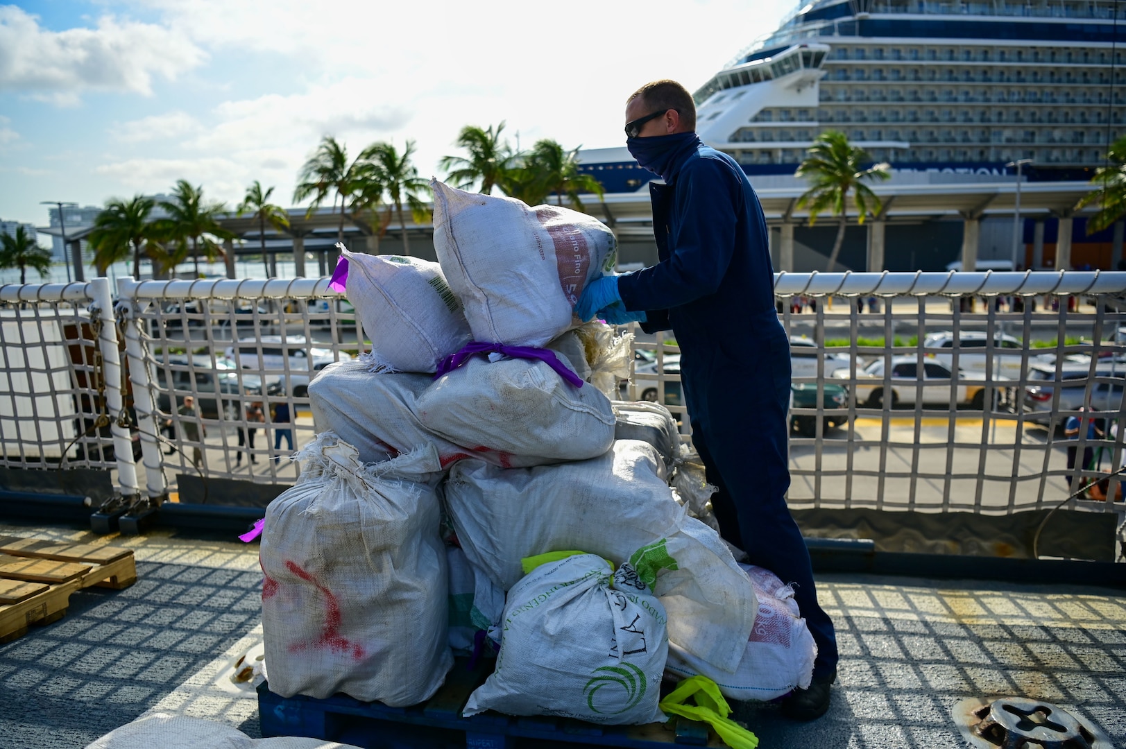A USCGC Mohawk (WMEC 913) crew member stacks bales of illegal narcotics on the flight deck of the cutter