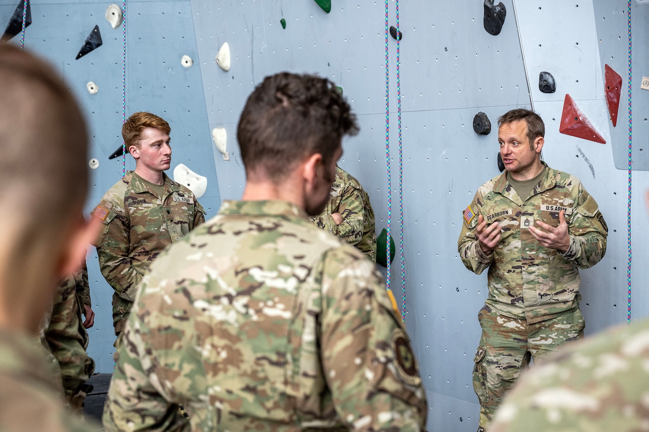 A man standing in front of a rock wall talks to others who are listening to him.