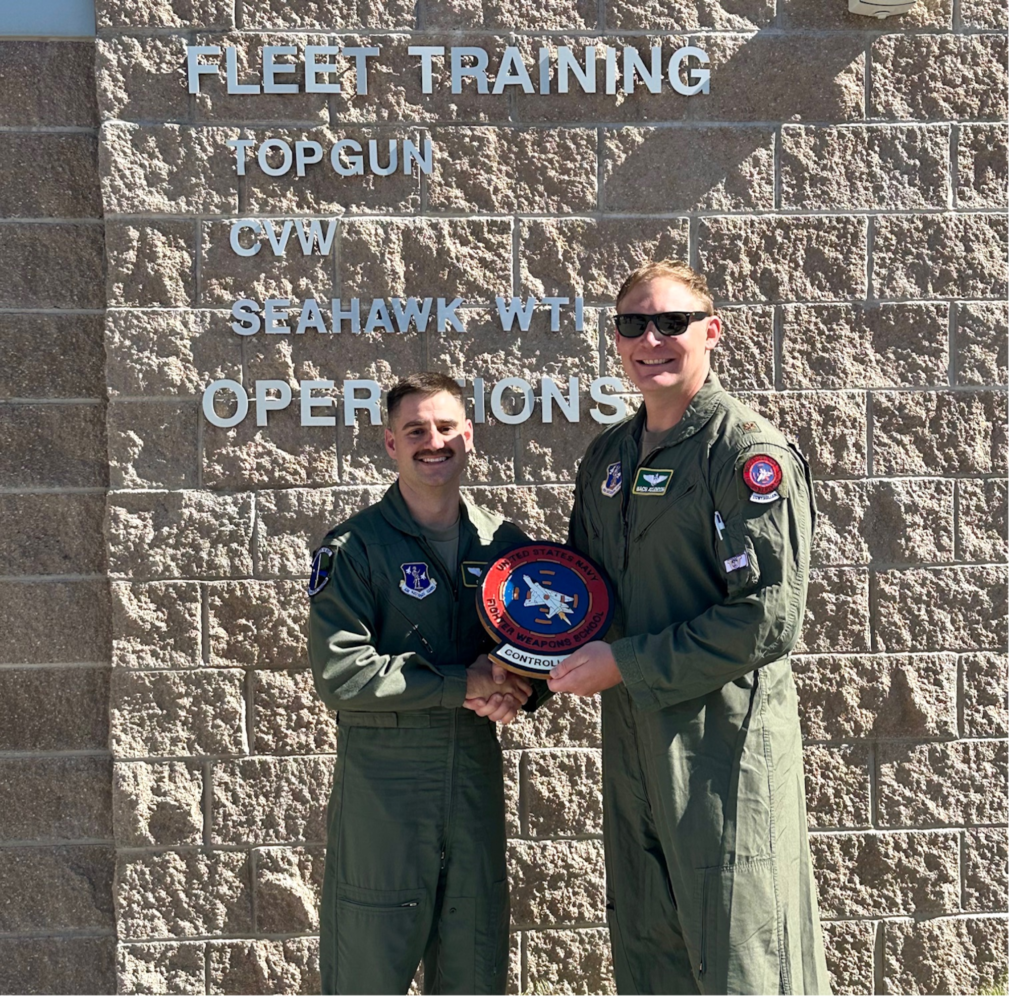 Two Airmen stand in front of the U.S. Navy TOPGUN sign