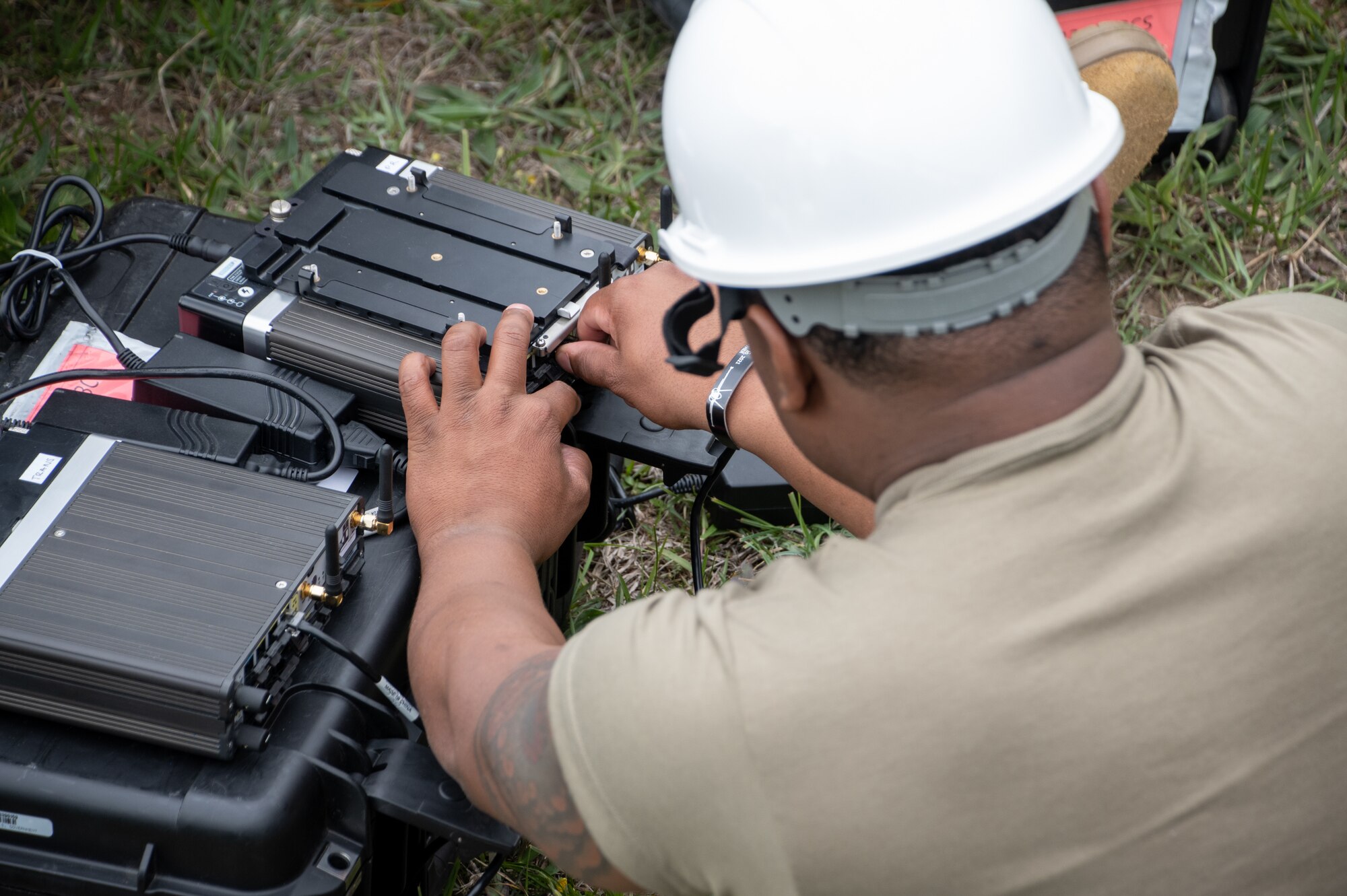 A U.S. Air National Guard Airman works with plugs and cables in black communications boxes.