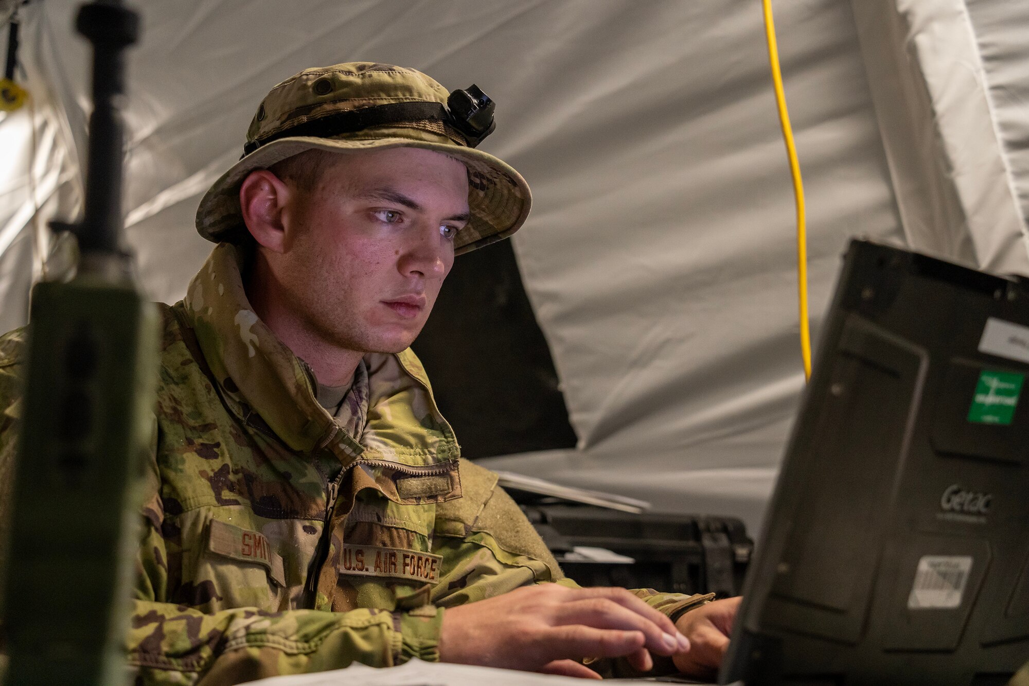 A U.S. Air National Guard Airman works on a computer in a field tent.