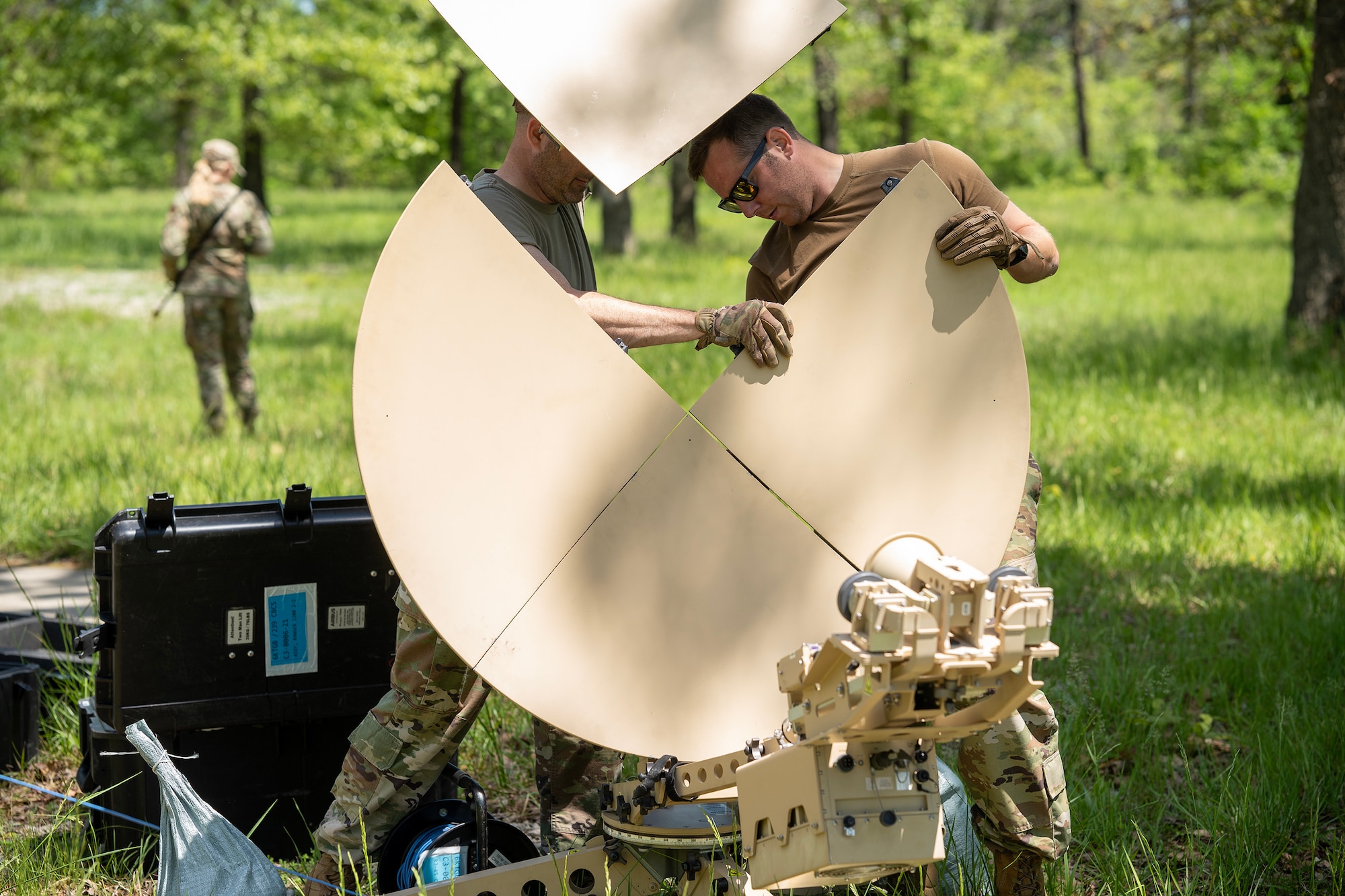 Two U.S. Air National Guard Airman work to erect a portable satellite receiver dish.