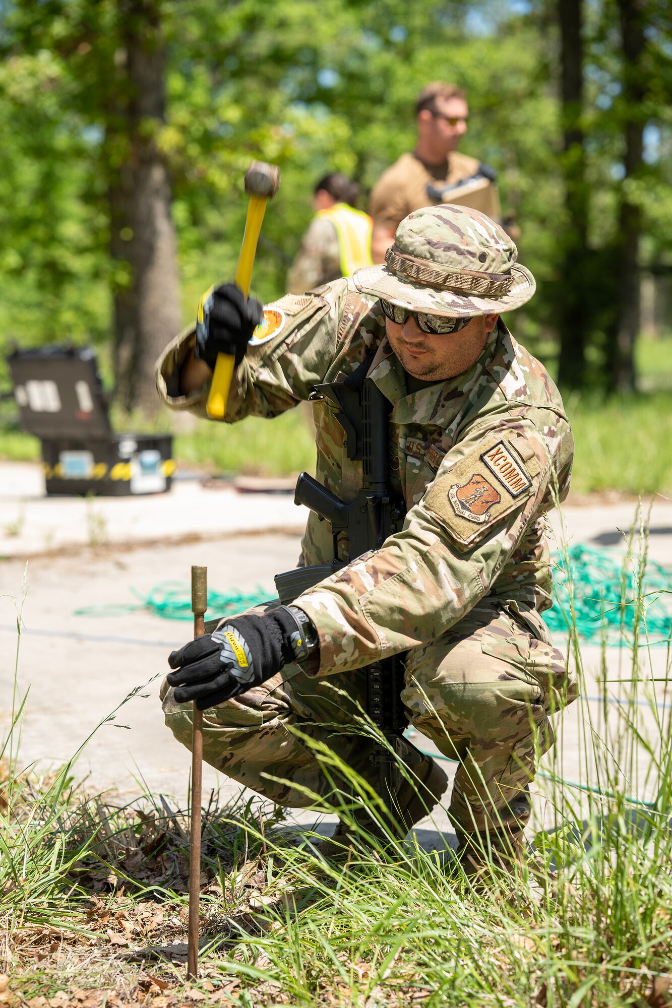 A U.S. Air National Guard Airman hammers in tent stakes with a small sledgehammer.