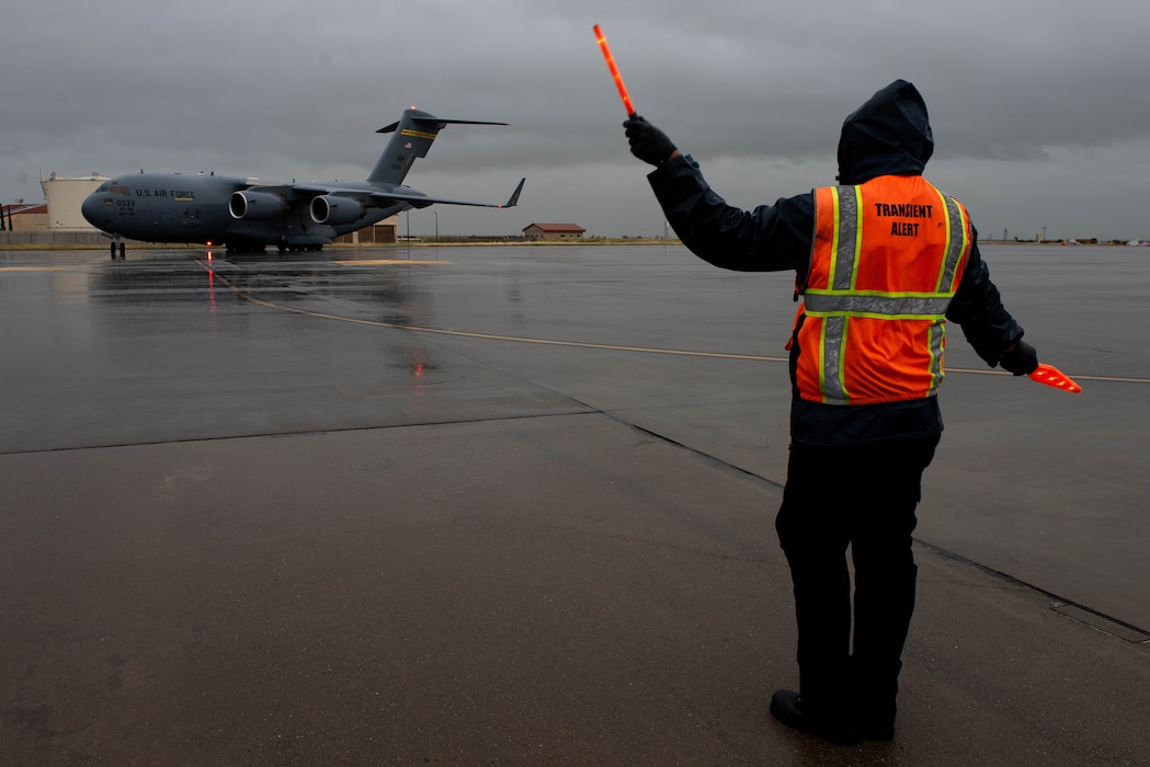 Service agent directs aircraft on flight line in the rain