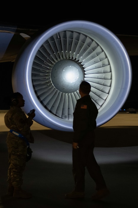 A pilot and crew chief check a KC-46 engine during a preflight inspection at night..