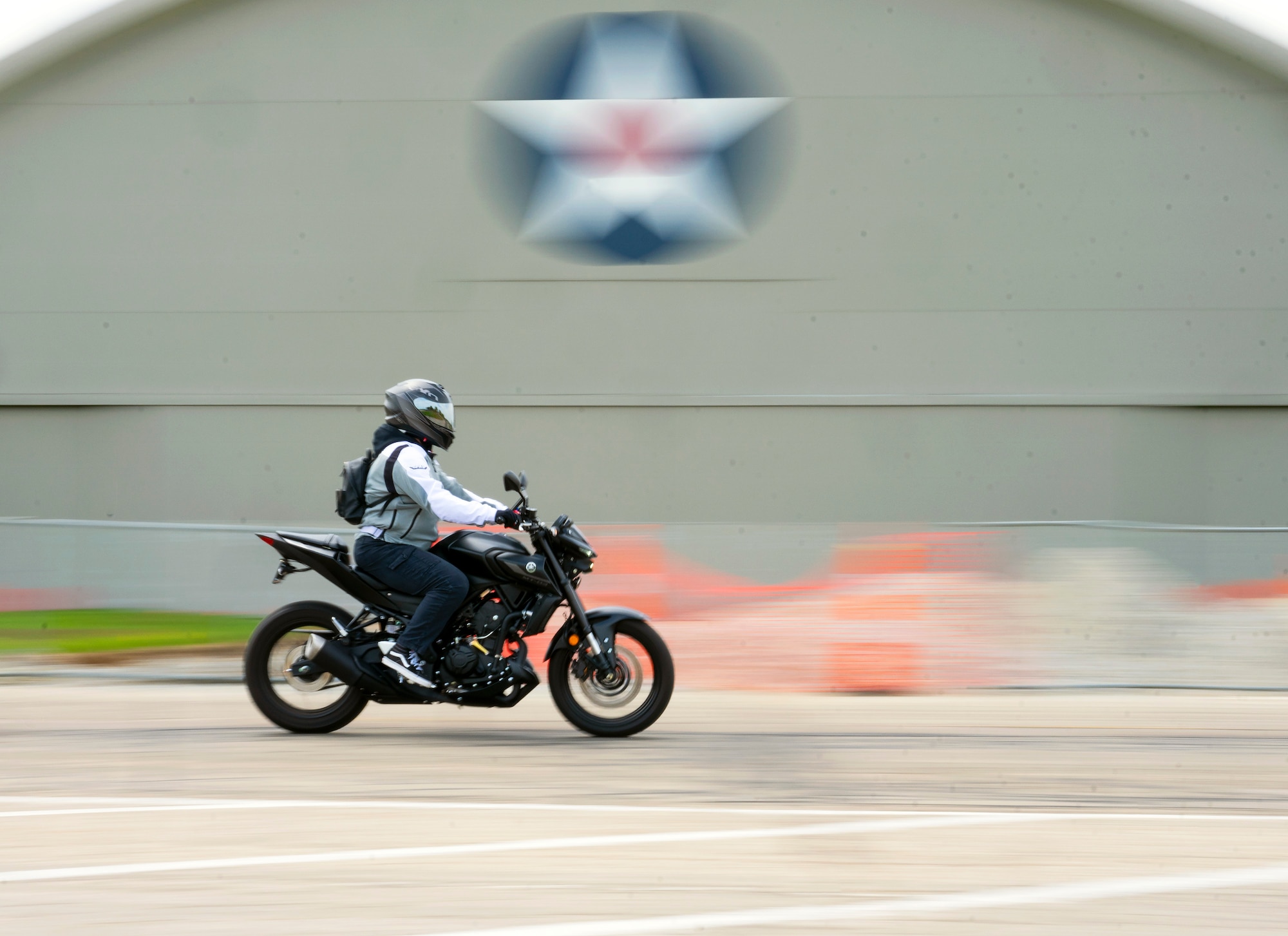 A panning shot of a motorcycle and rider going past the Air Force Museum. The bike is sharp, the museum is blurred with motion.