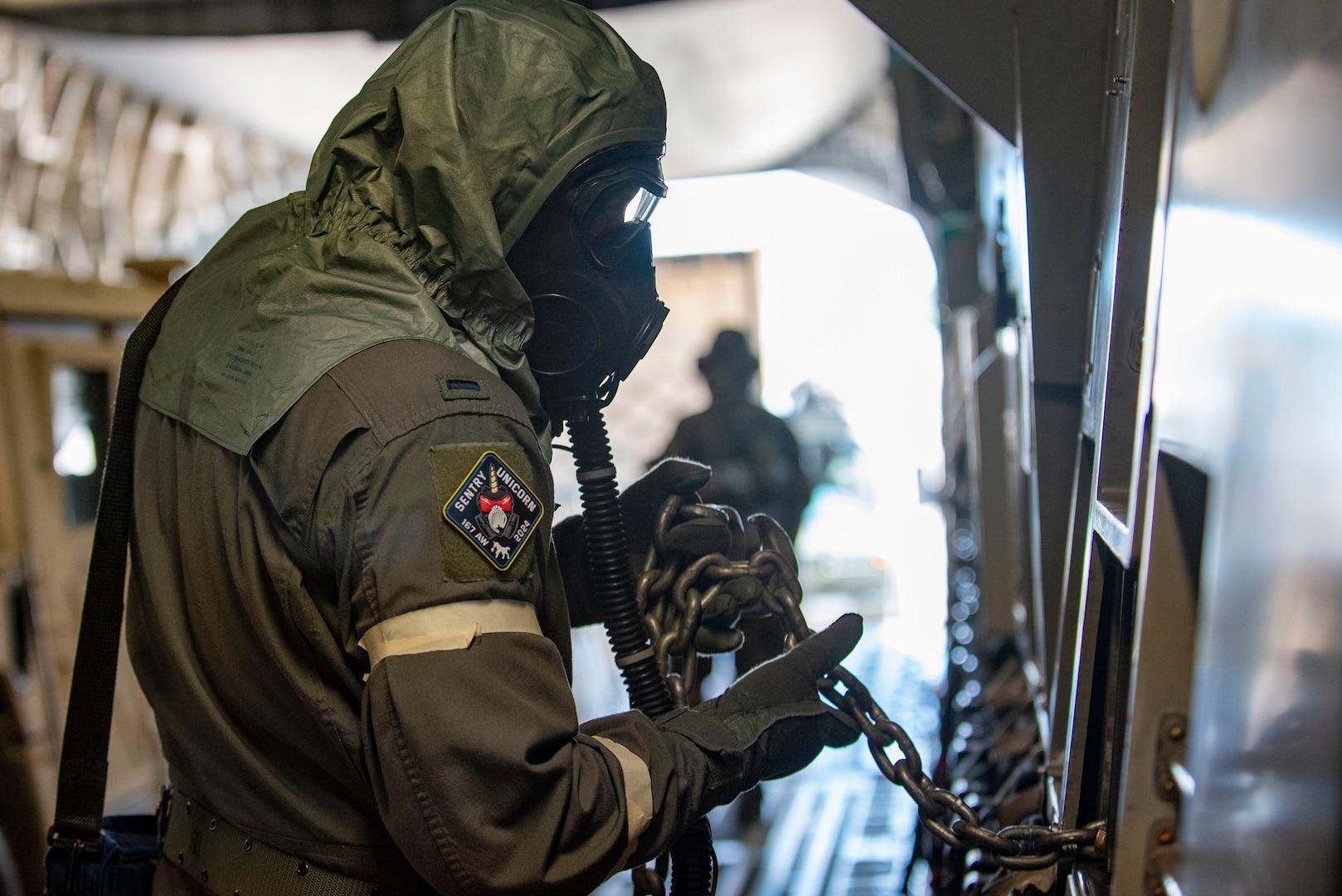 a man stand in chemical gear, holds a chain inside a cargo aircraft