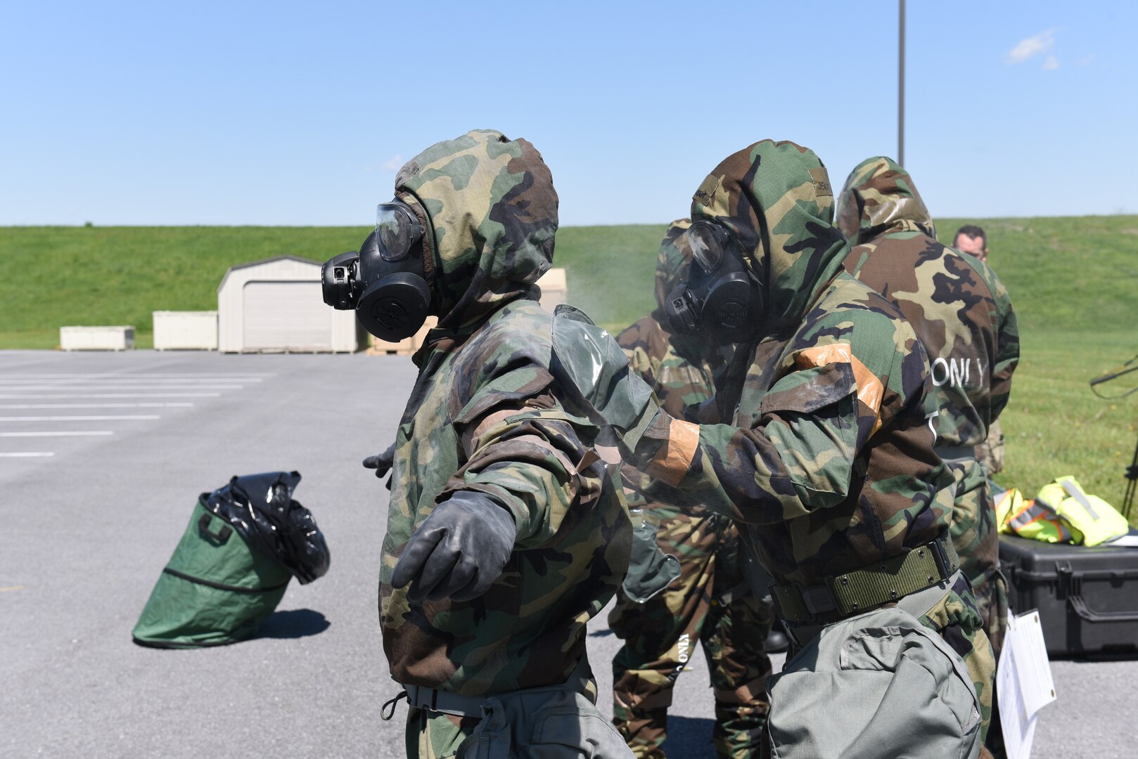 a person pats down the back of another person both are wearing chemical gear and masks