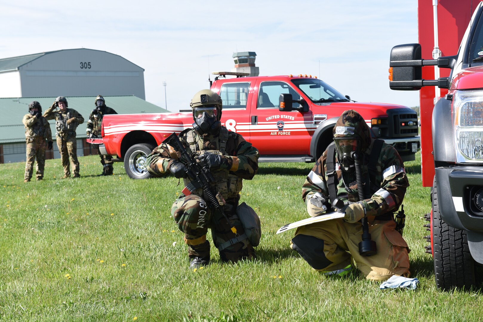 two people in chemical gear and masks kneel in the grass