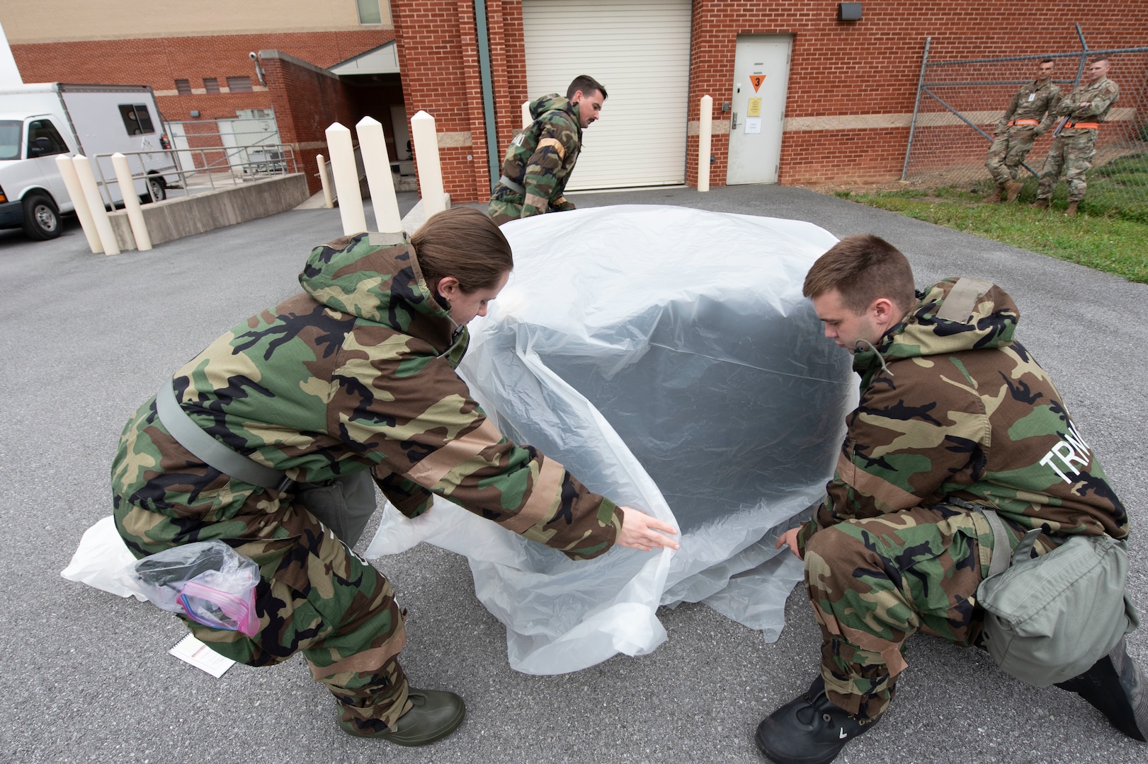 three people cover a piece of equipment with large sheet of plastic