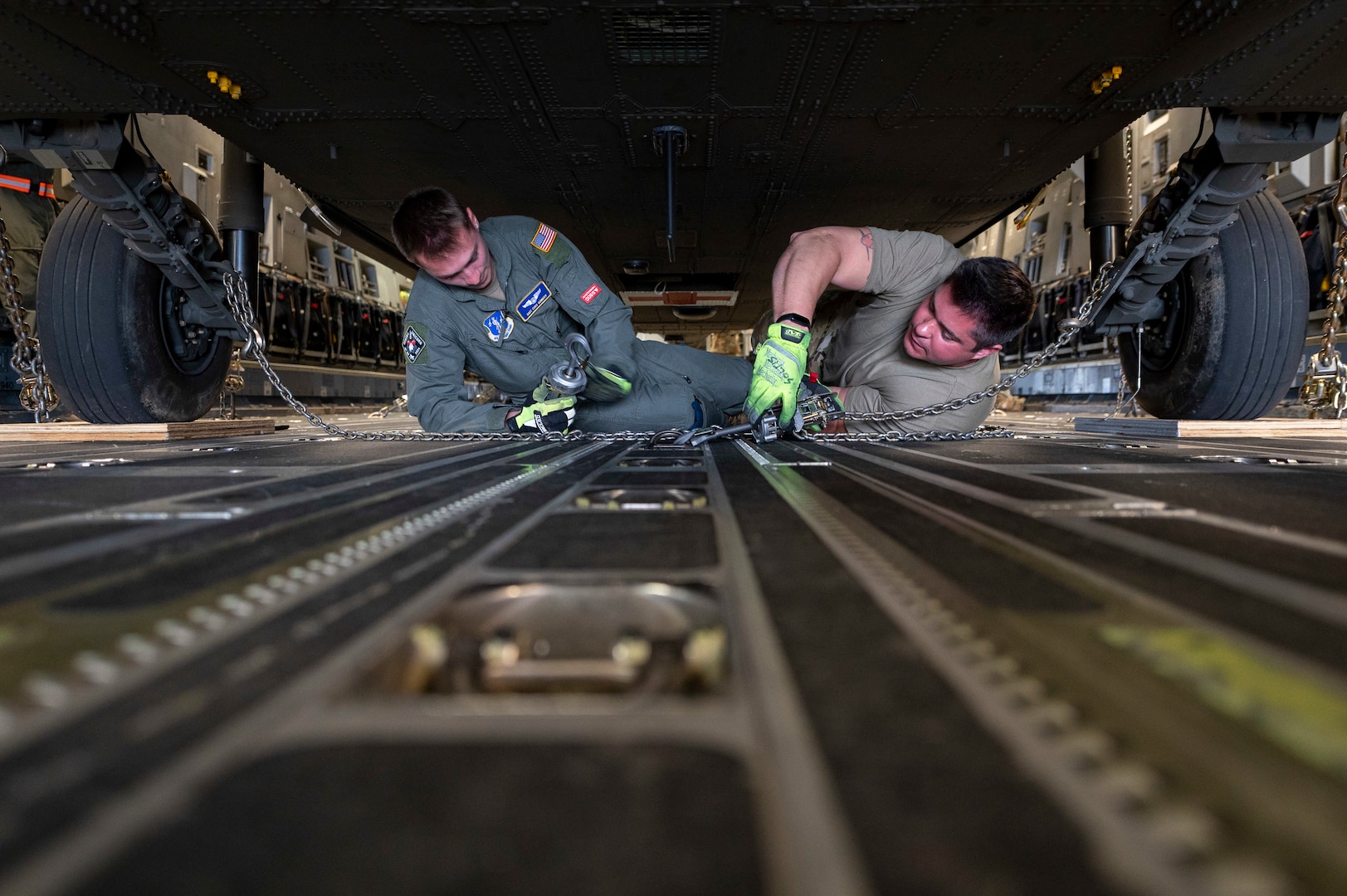 two men lay on the floor of an aircraft to attach chains to the floor