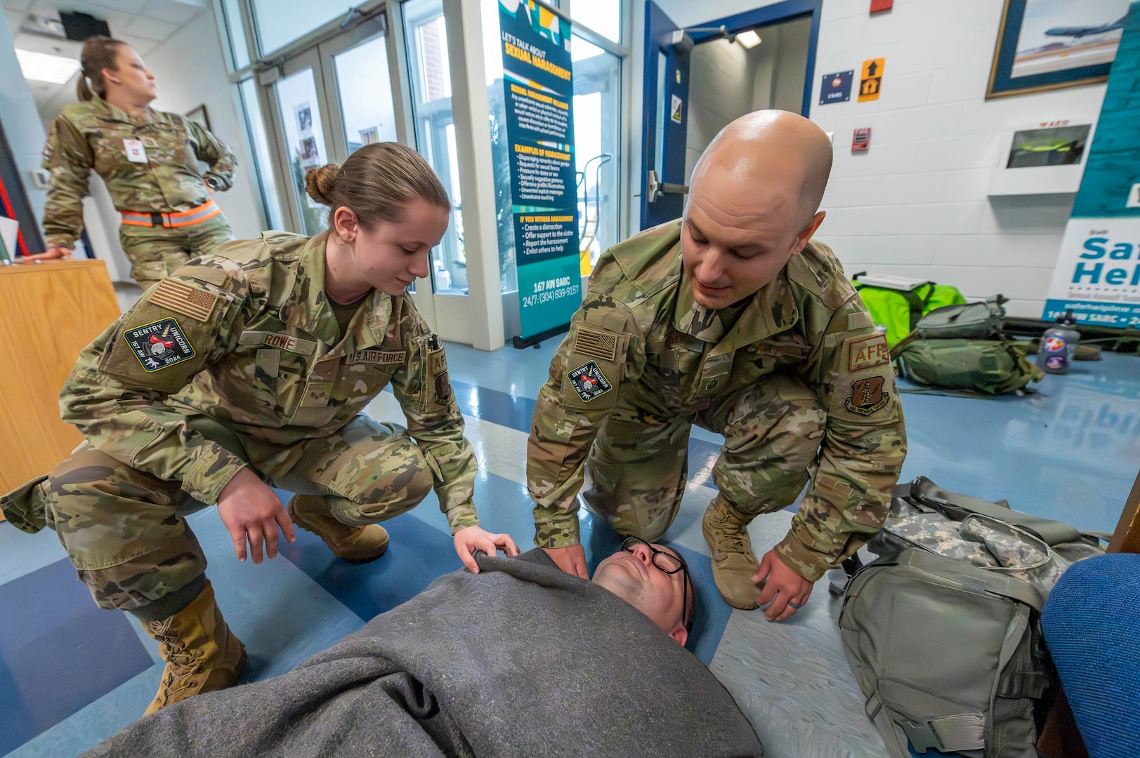 a woman and man kneel over another man laying on the floor