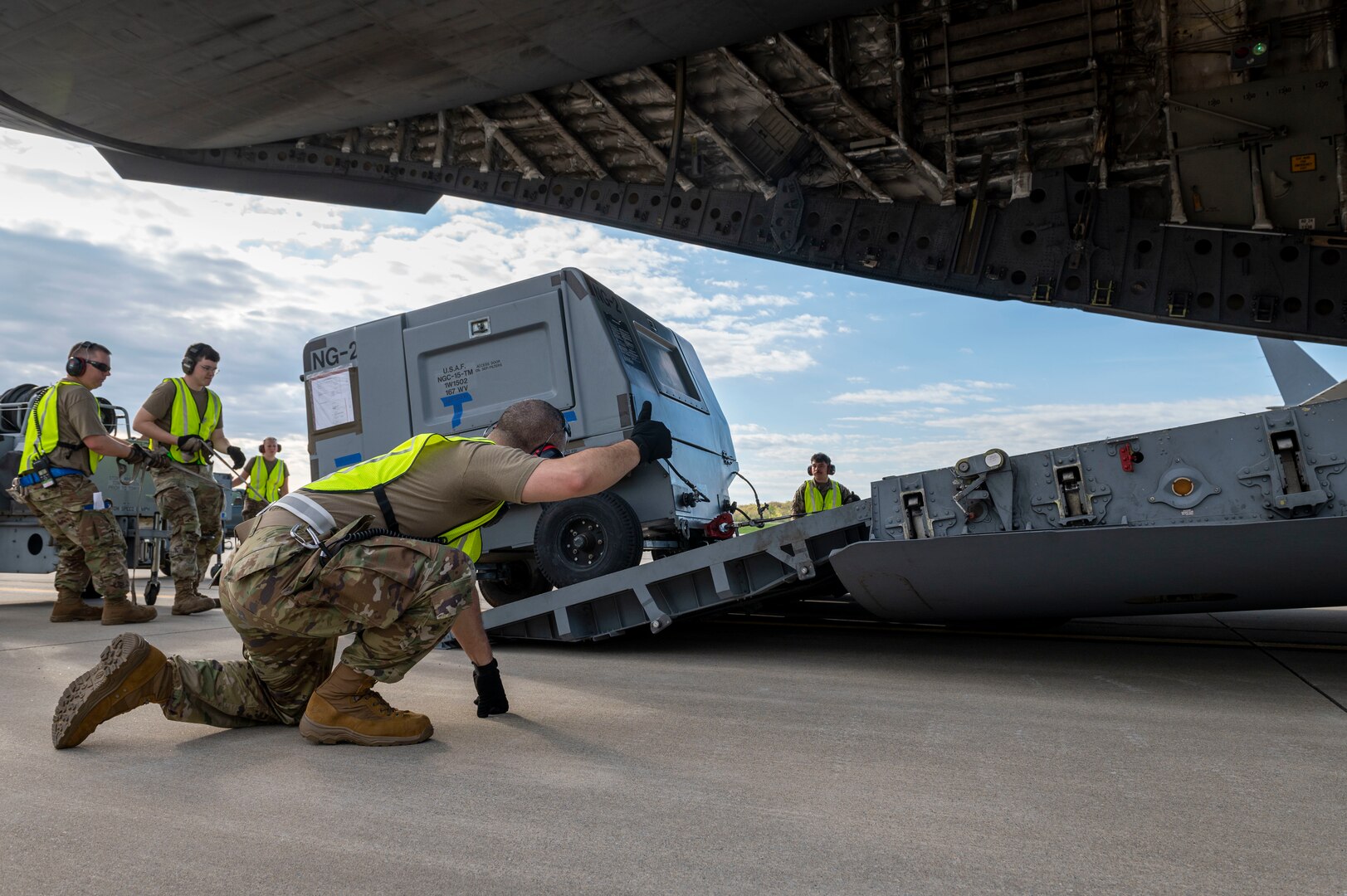 a man kneels on the ground as he watches a piece of equipment go up a ramp
