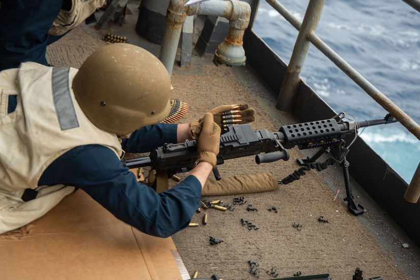 A sailor loads ammunition into a machine gun.