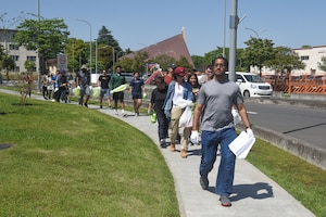 Group of participants with garbage bags walk in a single-file line down the sidewalk.