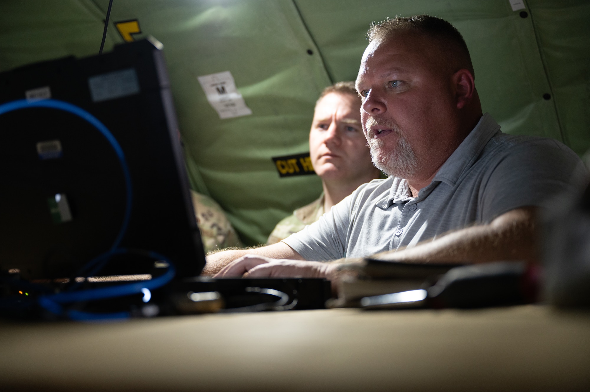 Shawn Moore, 46th Test Squadron Link 16 fielding team contractor, demonstrates a network capability on a computer  during a training. In the background, a man watching the screen.