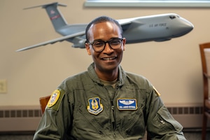 U.S. Air Force Senior Airman James Getonga poses for a photo, while wearing his flight suit uniform and sitting in front of a model C-5M Super Galaxy.