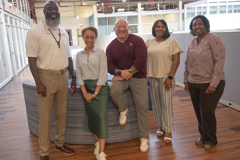 Five people pose for a photo indoors.