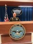 Army Soldier in official uniform stands behind Department of Defense seal in the Pentagon