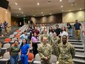 Four Army Soldiers in uniform stand with medical students in an auditorium