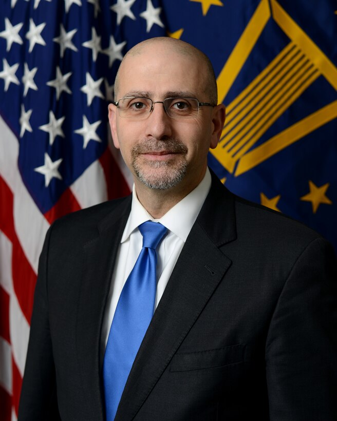 A photo of man in tie and suit in front of flags.