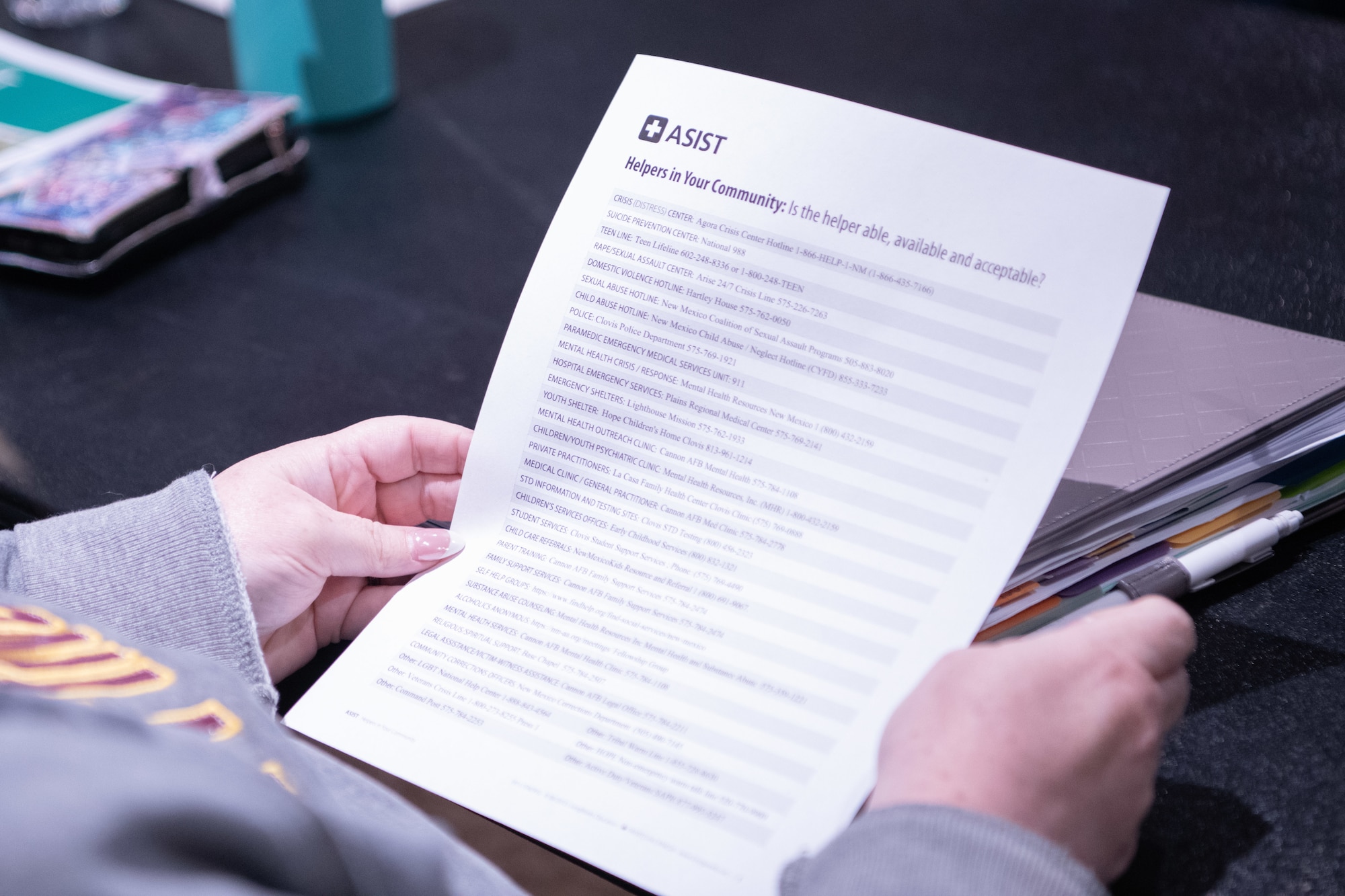 A participant of the Applied Suicide Intervention Skills Training (ASIST) workshop holds a list of resources available at Cannon Air Force Base, New Mexico, May 7, 2024. One objective of the ASIST workshop was to help attendees recognize other important aspects of suicide prevention, including the resources available locally. (U.S. Air Force photo by Senior Airman Drew Cyburt)